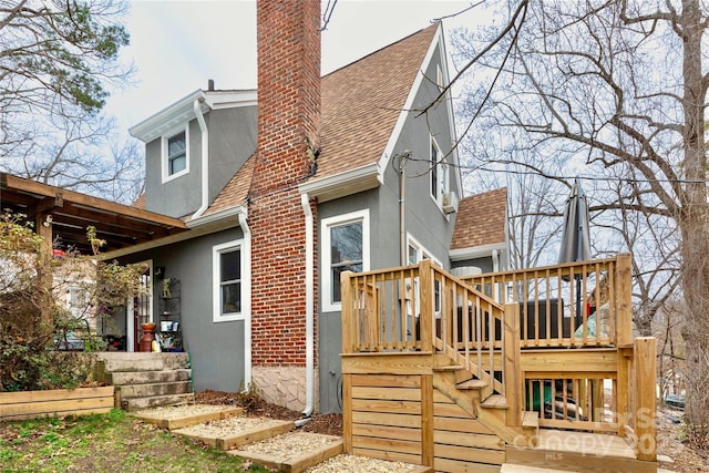 back of property with a shingled roof, a chimney, stairs, and stucco siding