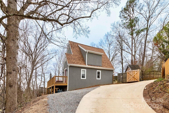 view of home's exterior with a shingled roof, a gate, fence, a wooden deck, and stucco siding