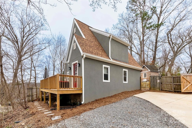 view of home's exterior featuring fence, roof with shingles, a wooden deck, a gate, and stucco siding