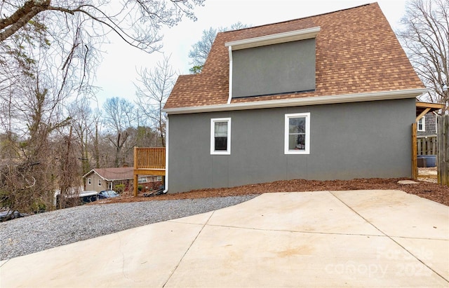 rear view of house featuring a patio, roof with shingles, and stucco siding