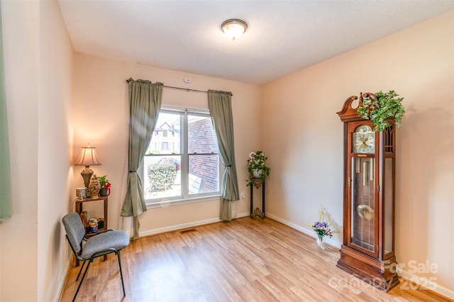 sitting room with visible vents, baseboards, light wood finished floors, and a textured ceiling