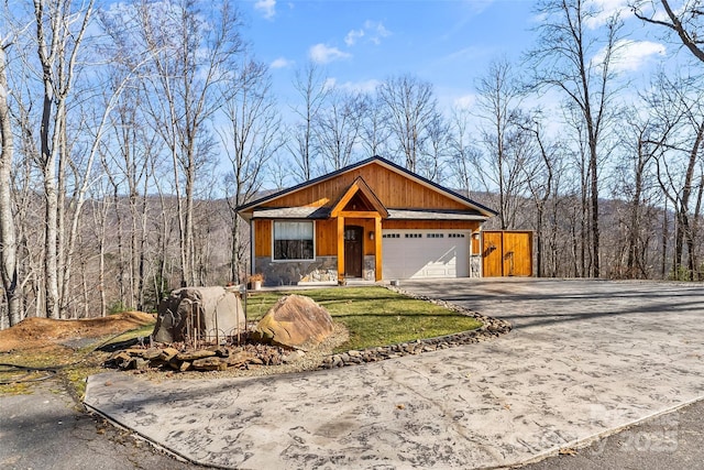 view of front of home with concrete driveway, an attached garage, a view of trees, and stone siding