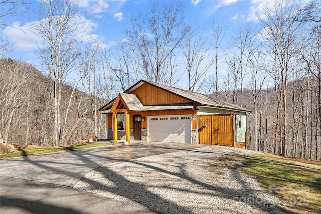 view of front of home with an attached garage, a forest view, gravel driveway, and a shingled roof