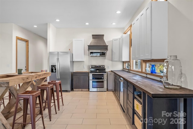 kitchen with wooden counters, custom range hood, recessed lighting, appliances with stainless steel finishes, and white cabinets