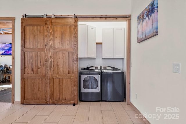 laundry room featuring washing machine and clothes dryer, cabinet space, baseboards, and a barn door