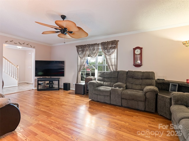 living room with stairway, baseboards, ceiling fan, crown molding, and light wood-type flooring