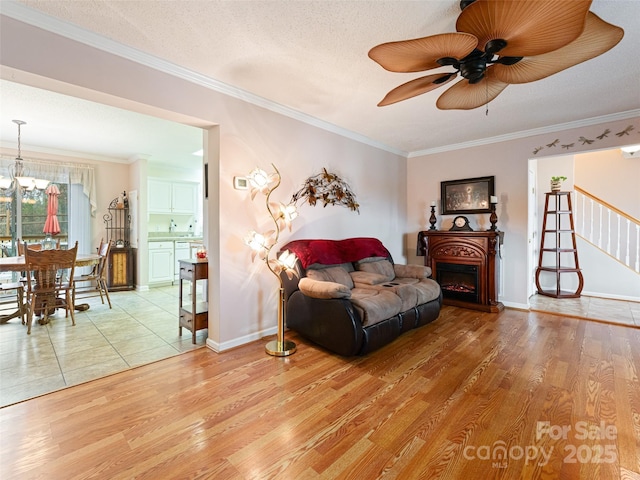 living area featuring stairs, light wood-style flooring, a fireplace, and ornamental molding