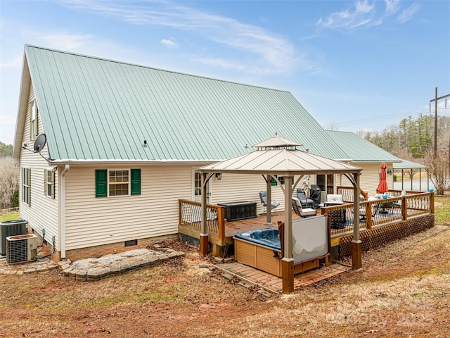 back of property featuring a wooden deck, a gazebo, an outdoor hot tub, crawl space, and metal roof