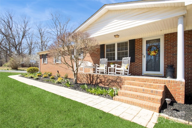 doorway to property featuring a yard, brick siding, and covered porch