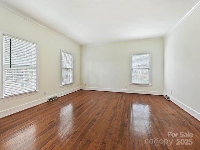 empty room featuring dark wood-style floors, ornamental molding, visible vents, and baseboards