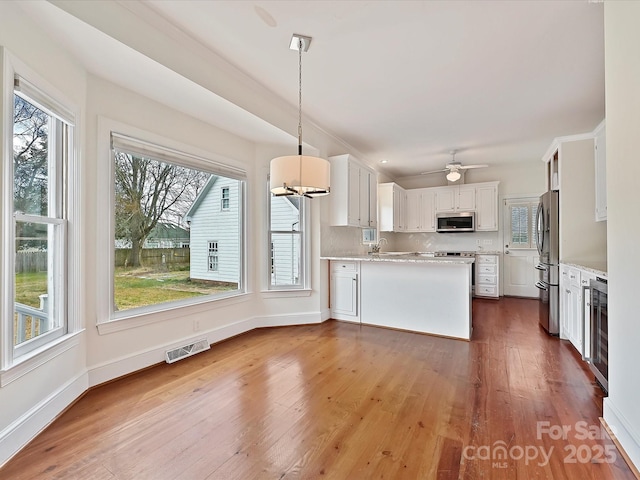 kitchen featuring visible vents, dark wood-type flooring, a peninsula, stainless steel appliances, and light countertops