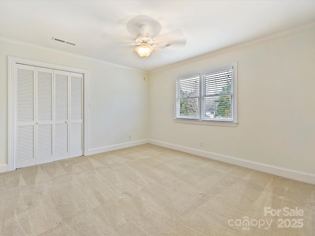 unfurnished bedroom with light colored carpet, visible vents, baseboards, a closet, and crown molding