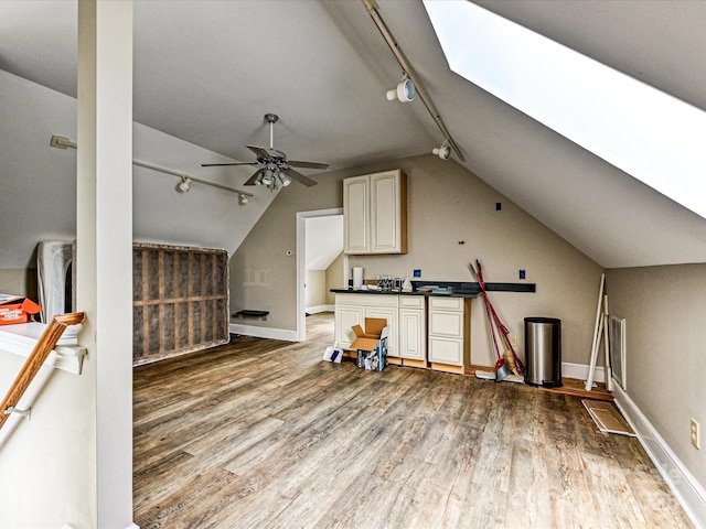 additional living space featuring lofted ceiling with skylight, wood finished floors, a ceiling fan, and baseboards