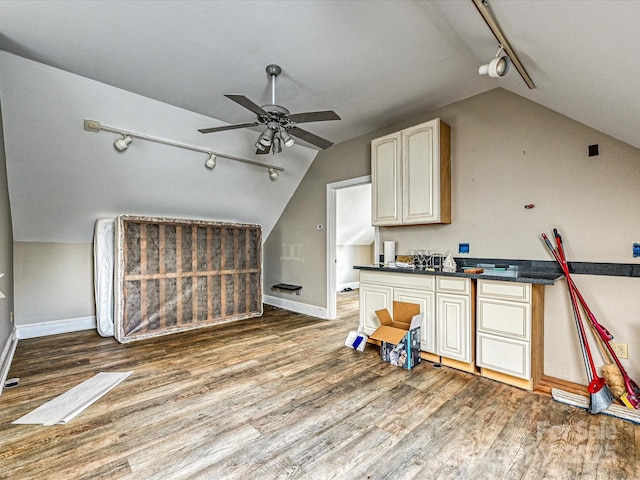 kitchen with lofted ceiling, wood finished floors, a ceiling fan, baseboards, and dark countertops