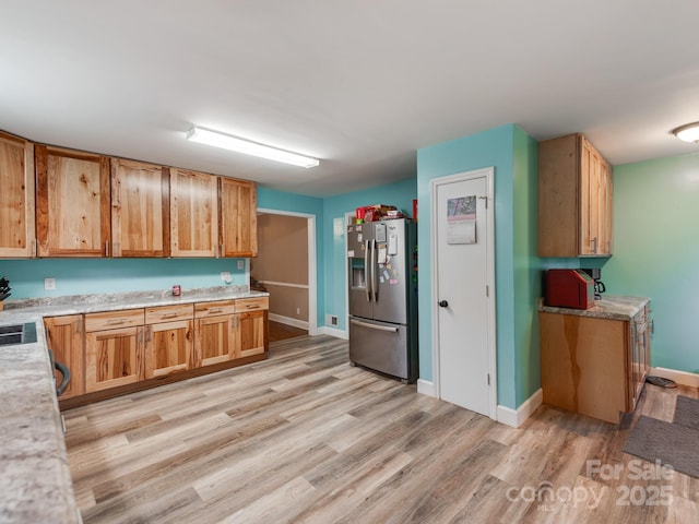 kitchen with light countertops, light wood finished floors, stainless steel fridge, and baseboards