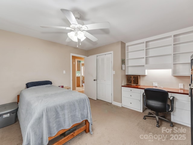 bedroom featuring ceiling fan, built in desk, a closet, and light colored carpet