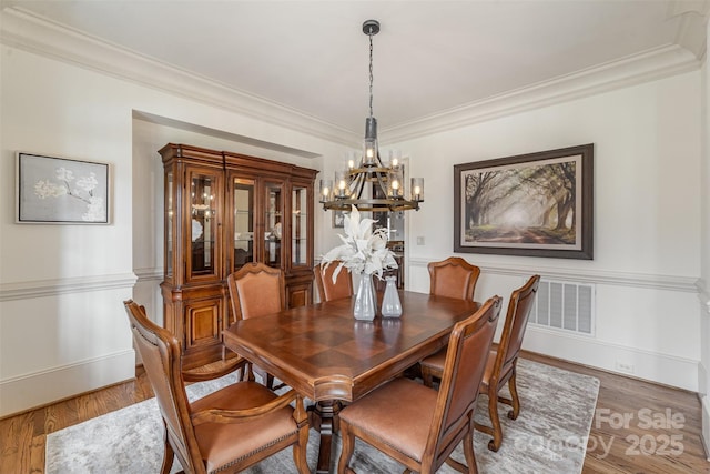 dining room featuring an inviting chandelier, crown molding, light wood-style floors, and wainscoting