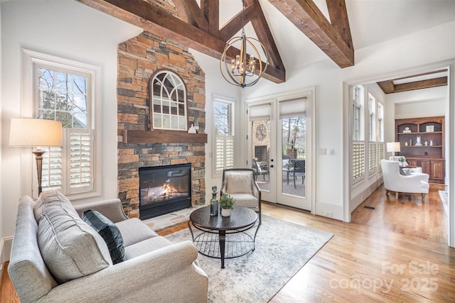 living area featuring beamed ceiling, a fireplace, french doors, an inviting chandelier, and wood finished floors