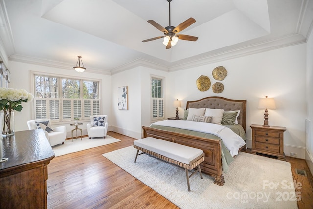 bedroom with a tray ceiling, visible vents, wood finished floors, and ornamental molding