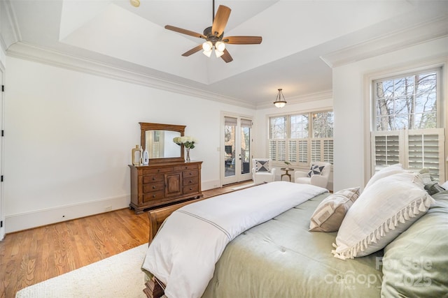 bedroom featuring a raised ceiling, ornamental molding, wood finished floors, french doors, and baseboards