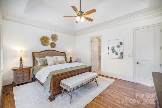 bedroom featuring a raised ceiling, light wood-style floors, visible vents, and ornamental molding