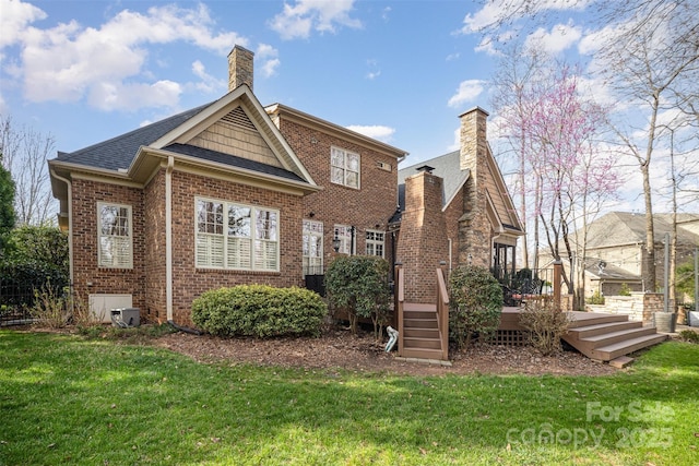 rear view of house with roof with shingles, a chimney, a deck, a lawn, and brick siding