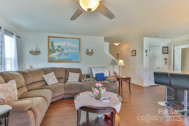 living room with ceiling fan, baseboards, and wood finished floors