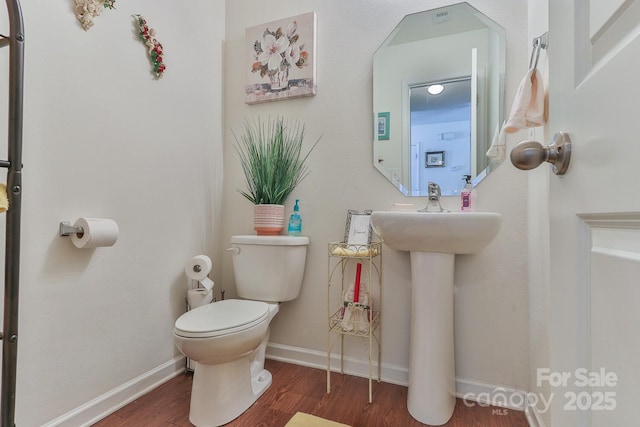 half bathroom featuring wood finished floors, toilet, and baseboards