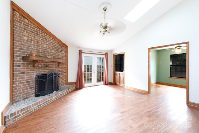 unfurnished living room featuring french doors, a ceiling fan, a brick fireplace, wood finished floors, and vaulted ceiling with skylight