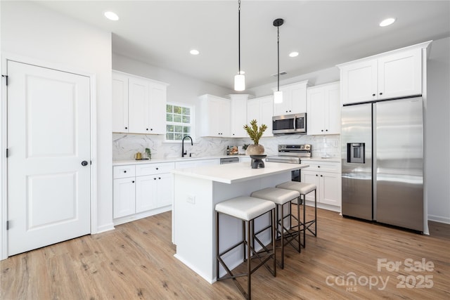 kitchen featuring light wood finished floors, appliances with stainless steel finishes, a kitchen island, and a kitchen breakfast bar