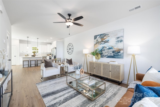 living area with baseboards, light wood finished floors, ceiling fan, and visible vents