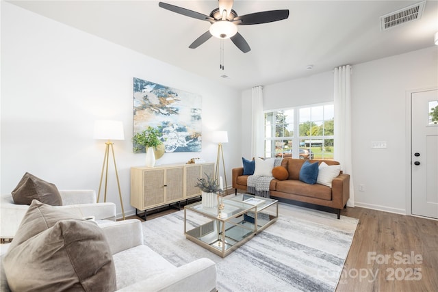 living room with baseboards, visible vents, wood finished floors, and a ceiling fan