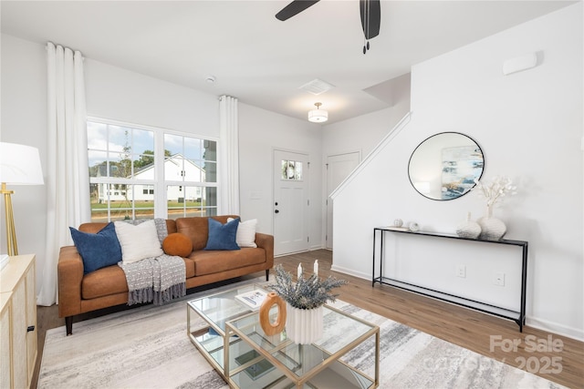 living area with baseboards, visible vents, wood finished floors, and a ceiling fan