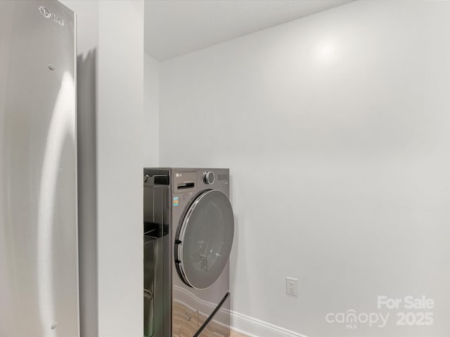 clothes washing area with light wood-type flooring, baseboards, and washing machine and clothes dryer