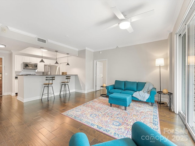 living room featuring dark wood-style flooring, visible vents, crown molding, and baseboards