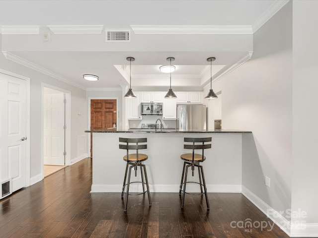 kitchen with visible vents, dark countertops, appliances with stainless steel finishes, a kitchen bar, and white cabinetry