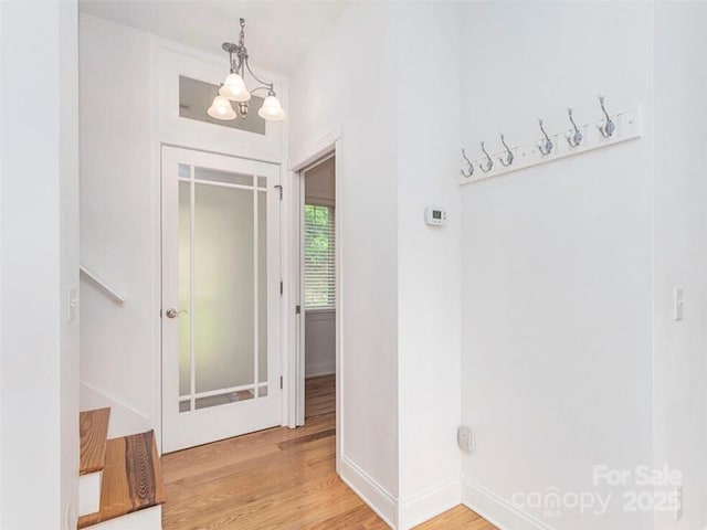 hallway featuring baseboards, a notable chandelier, and light wood finished floors