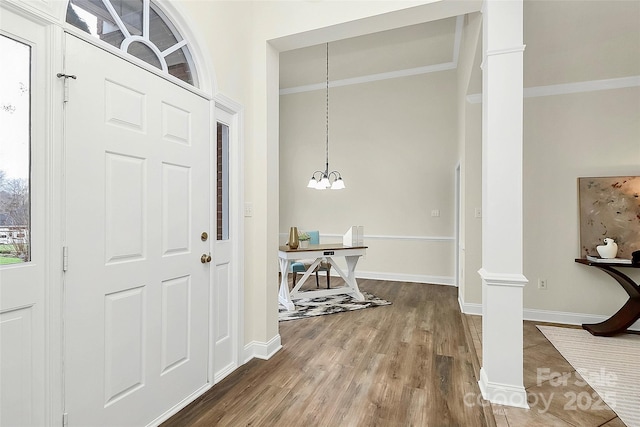 entryway with crown molding, baseboards, an inviting chandelier, wood finished floors, and ornate columns