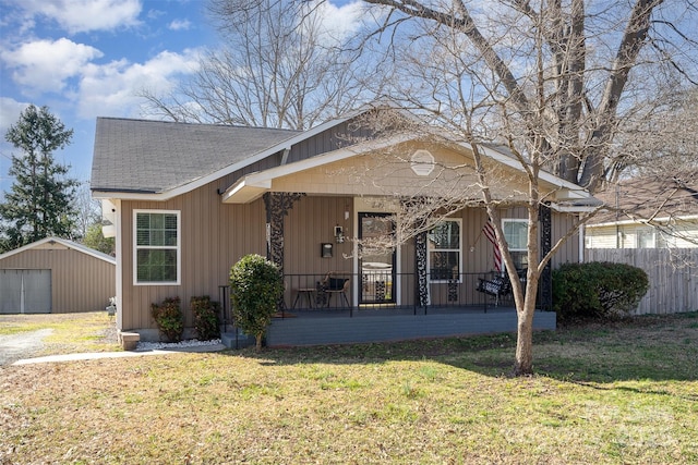 bungalow-style house featuring a shingled roof, covered porch, board and batten siding, fence, and a front lawn