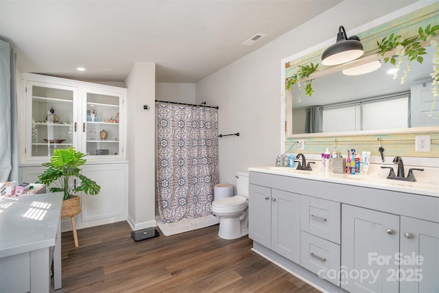 bathroom with toilet, double vanity, a sink, and wood finished floors