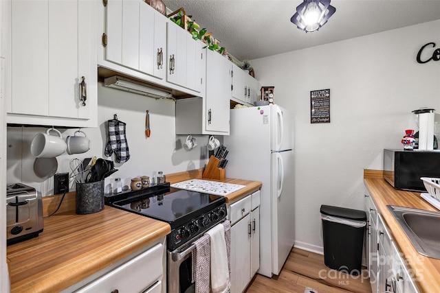 kitchen with black microwave, light wood-style floors, wooden counters, freestanding refrigerator, and stainless steel electric range oven