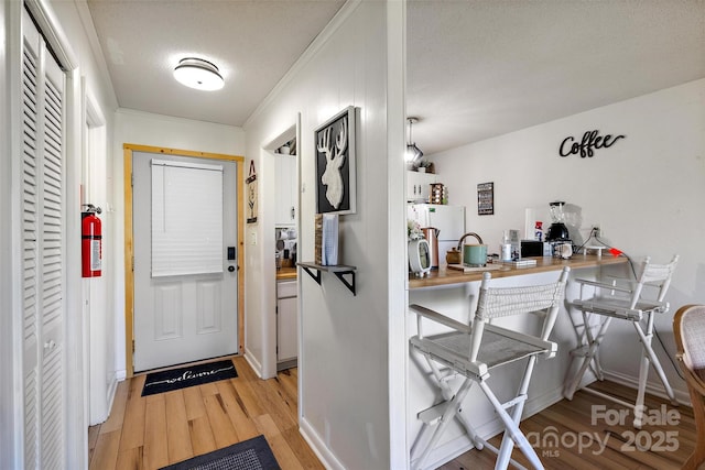 entrance foyer with a textured ceiling, crown molding, light wood-style flooring, and baseboards