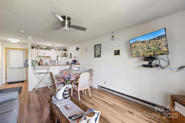 dining space with a ceiling fan, a baseboard radiator, light wood-style flooring, and a textured ceiling