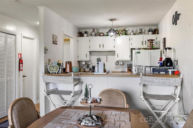 kitchen with a peninsula, white cabinetry, crown molding, and freestanding refrigerator