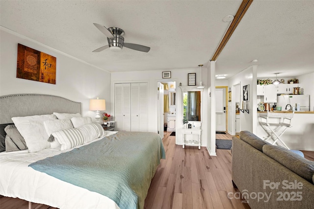 bedroom featuring a closet, light wood-style flooring, freestanding refrigerator, connected bathroom, and a textured ceiling