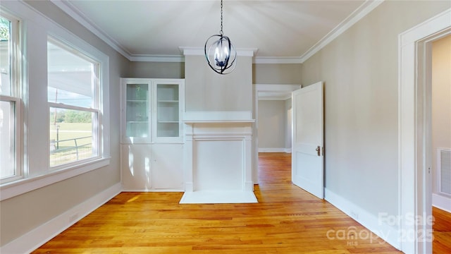 unfurnished dining area featuring a chandelier, ornamental molding, and light wood-type flooring
