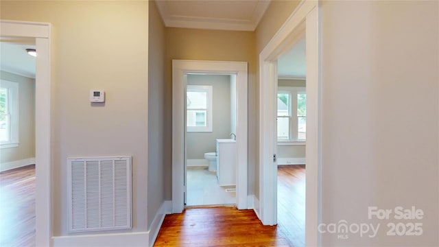 hallway featuring baseboards, visible vents, ornamental molding, and wood finished floors