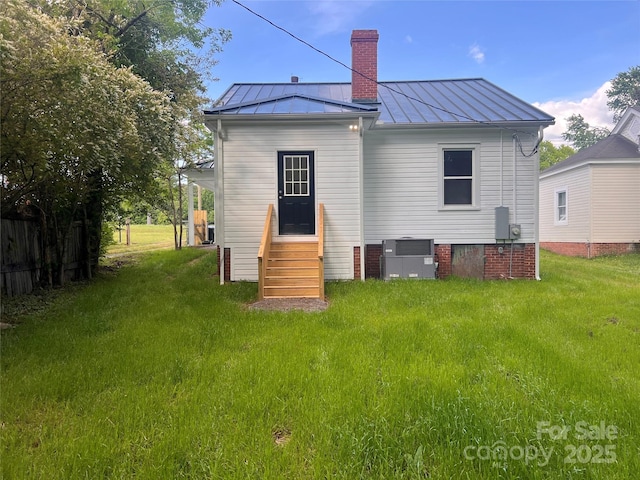 rear view of house featuring a lawn, a standing seam roof, a chimney, and entry steps