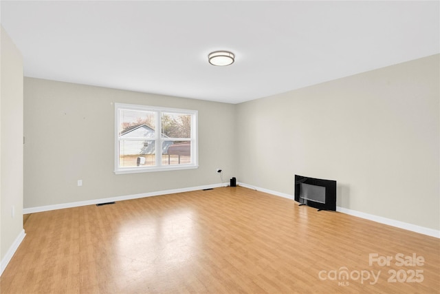 spare room featuring baseboards, a fireplace, visible vents, and wood finished floors