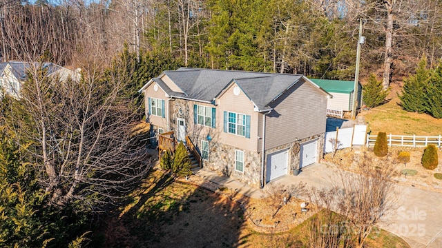 exterior space with a garage, fence, stone siding, driveway, and stairway